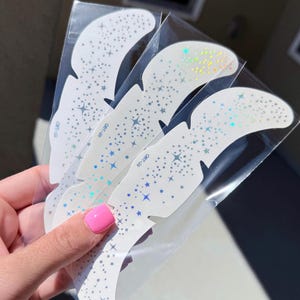 Peut inclure: Une tasse en céramique blanche avec une anse noire et l'inscription "But First, Coffee" en gras noir. La tasse est posée sur un fond flou, suggérant un cadre chaleureux.