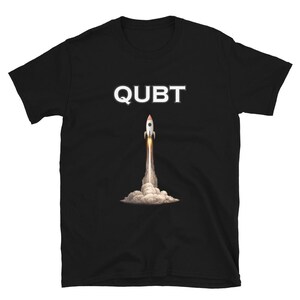 May include: Black t-shirt with the word "QUBT" in white block letters above a graphic of a rocket launching into space. The rocket is white, orange, and gray, with a trail of smoke and fire.