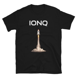 Può includere: T-shirt nera con la scritta "IONQ" in bianco sopra una grafica di un razzo in fase di lancio. Il razzo è bianco con dettagli rossi e neri, con una scia di fuoco e fumo.