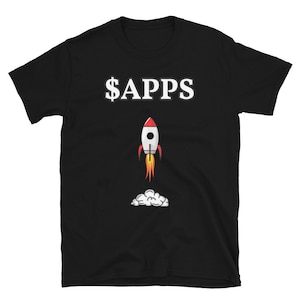 以下が含まれることがあります： 白い文字で「$APPS」と書かれた黒いTシャツ。白いボディと赤いフィンを持つ漫画のロケットが白い雲に向かって打ち上げられている。