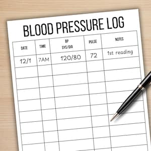May include: A white blood pressure log sheet with the title "BLOOD PRESSURE LOG" at the top. The log includes columns for date, time, BP, pulse, and notes. A black pen with silver accents rests on the sheet, ready for use. The first entry shows a reading of 120/80.