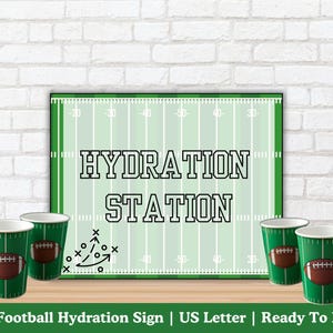 May include: A green sign with the words "HYDRATION STATION" in black, resembling a football field. Six green cups with football graphics are arranged in front of the sign. The sign also has a football play diagram.