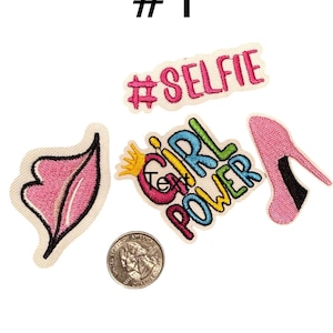 May include: A collection of embroidered patches including a pink lip shape, a pink high-heeled shoe, and text patches reading #SELFIE and GIRL POWER with a yellow crown. A US quarter coin is included for scale, measuring 0.955 inches in diameter.