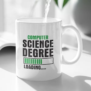 Può includere: Una tazza di ceramica bianca con la scritta "COMPUTER SCIENCE DEGREE LOADING...." in verde e nero. L'acqua viene versata nella tazza da una brocca scura. Una pianta verde è sullo sfondo.