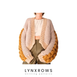 Puede incluir: Un cárdigan de punto en color rosa y mostaza. El cárdigan es corto y presenta un patrón de punto trenzado en las mangas.