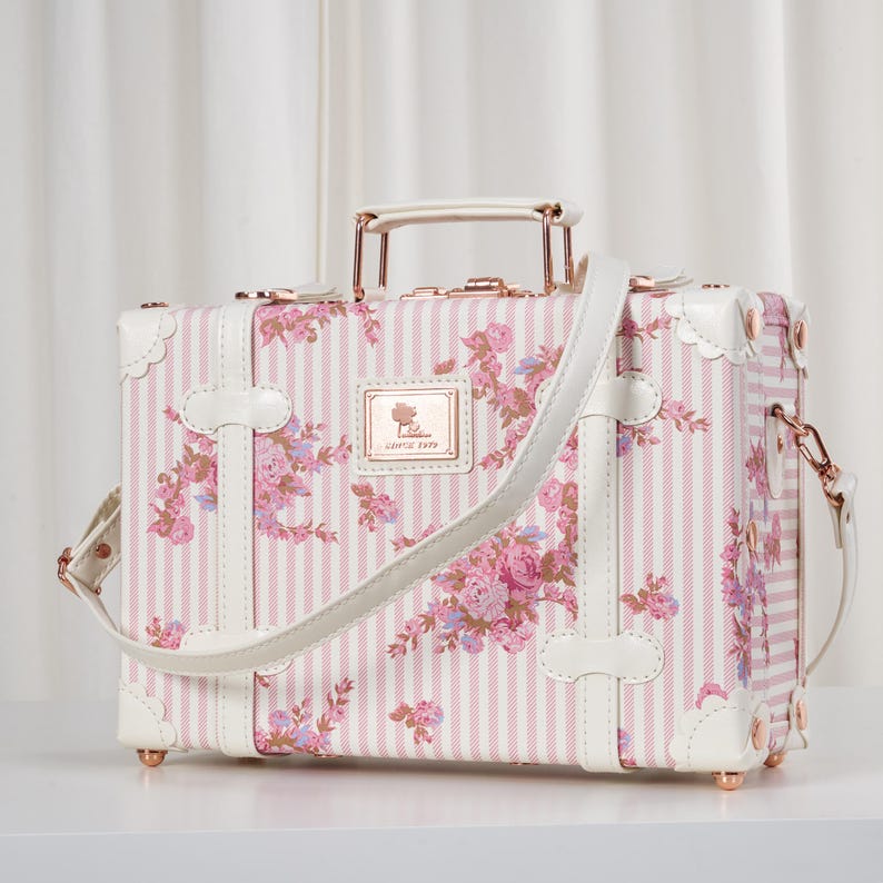 May include: A white vintage-style train case with brown leather accents and a metal latch. The case is shown in three different positions: closed, open, and with a short strap attached to a handle. The text 'Multifunctional Train Case' is above the case. The text 'Long Strap(used as shoulder bag)' is below the case with the long strap. The text 'Short Strap(fastened to suitcase)' is below the case with the short strap.