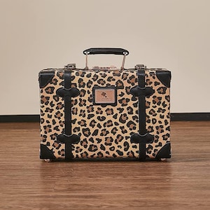 May include: A small, vintage-style suitcase with a leopard print design. The suitcase has black leather accents and a brass lock.