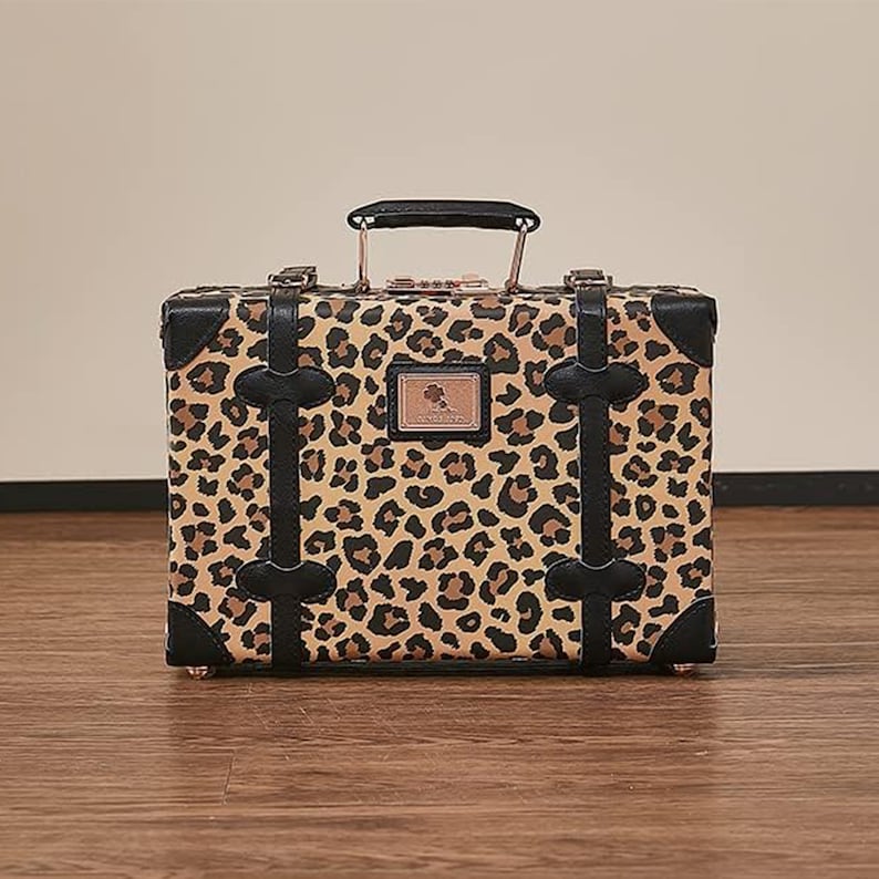 May include: A small, vintage-style suitcase with a leopard print design. The suitcase has black leather accents and a brass lock.