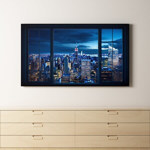 May include: A black framed canvas print of a cityscape at night, with a view of skyscrapers and a cloudy sky. The print is hanging on a white wall above a light wood dresser with six drawers.