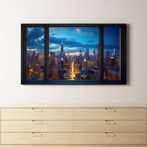 May include: A framed photograph of a city skyline at night, with a tall building in the center. The photograph is hanging on a white wall above a light wood dresser with three drawers.