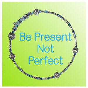 May include: A silver-toned bracelet with blue and silver beads, and decorative silver orbs. The bracelet is set against a bright green background with the words "Be Present Not Perfect" in blue.