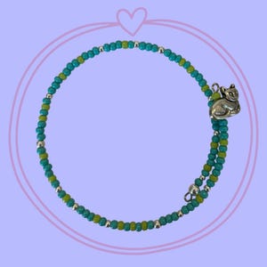 May include: A wrap bracelet featuring alternating turquoise and lime green seed beads, accented with small silver-toned metallic beads. A silver-toned metal charm shaped like a sitting cat is attached to one end of the circular beaded strand.