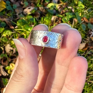 May include: A silver ring with a textured band and a red gemstone set in the center.