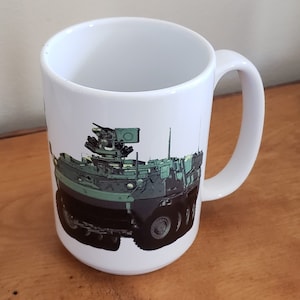May include: White ceramic coffee mug featuring a green military vehicle printed on the front. The vehicle has a large gun turret on top.