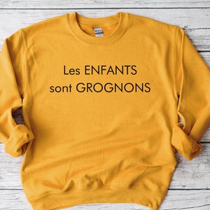May include: A mustard yellow sweatshirt with the text "Les ENFANTS sont GROGNONS" printed in black.