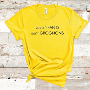May include: Yellow t-shirt with black text that reads "Les ENFANTS sont GROGNONS".