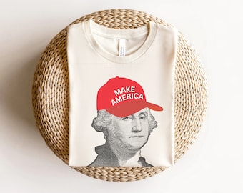 Puede incluir: Una camiseta blanca con un gráfico de George Washington usando un sombrero rojo "Make America".