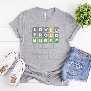 May include: Gray t-shirt with the words "Loved Proud Bubbe" in a grid pattern. The words are in different colors: yellow, green, and gray.