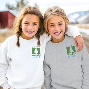 May include: A white crewneck sweatshirt and a heather gray crewneck sweatshirt, each featuring a green square logo on the left chest. The logo displays a white pine tree, the text CAMP WALDEN, and three light blue wavy lines underneath.