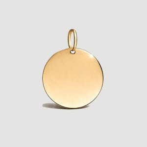 May include: A gold-coloured, circular pendant with a small loop at the top for a chain. The pendant has a smooth, reflective surface, likely made of metal. The design is simple and elegant.