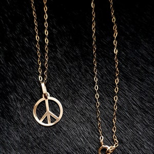 May include: A gold chain necklace with a peace sign pendant. The chain is made of small, linked circles.
