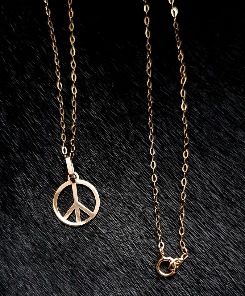 May include: A gold chain necklace with a peace sign pendant. The chain is made of small, linked circles.