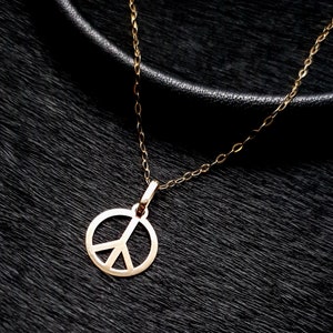 May include: A gold peace sign pendant necklace on a black background.
