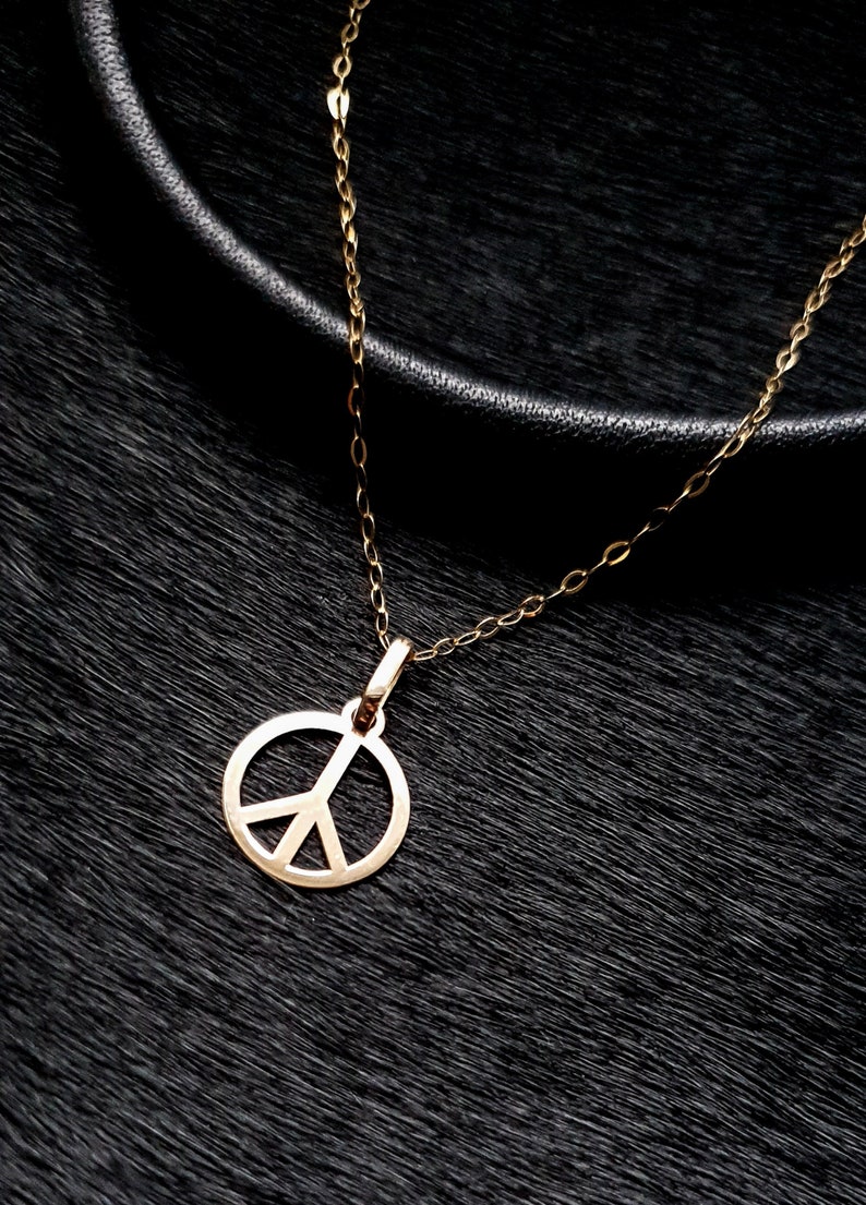 May include: A gold peace sign pendant necklace on a black background.