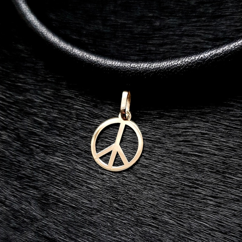 May include: A gold peace sign pendant necklace on a black leather cord.