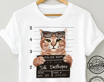 Op de afbeelding: Wit T-shirt met een kat met een zonnebril, geposeerd voor een politiefoto. De kat houdt een bord vast met de tekst "Sofa Destroyer". Het shirt bevat de tekst "POLICE DEPT." en "PREMIUM Quality GUARANTEED."