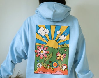 May include: Light blue hoodie with a colorful graphic on the back. The graphic features a retro design of a sun, clouds, flowers, and a butterfly in a landscape scene. The hoodie has a hood and long sleeves.
