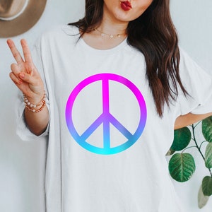 Puede incluir: Camiseta blanca con un símbolo de la paz en degradado de rosa a azul. El gráfico es un diseño audaz en una parte superior de ajuste holgado. Una prenda sencilla e informal.