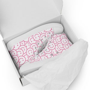 Peut inclure: Baskets montantes blanches avec un motif de visages souriants roses dans une bo&icirc;te blanche. Les baskets ont des lacets blancs et une semelle blanche. La bo&icirc;te est doubl&eacute;e de papier de soie blanc.