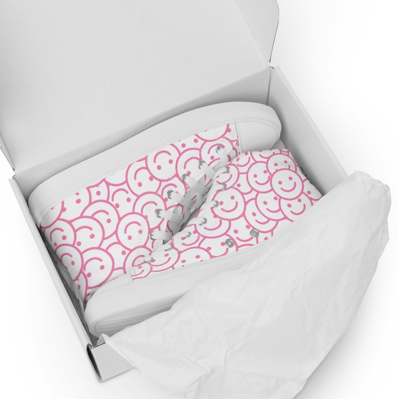 Peut inclure: Baskets montantes blanches avec un motif de visages souriants roses dans une bo&icirc;te blanche. Les baskets ont des lacets blancs et une semelle blanche. La bo&icirc;te est doubl&eacute;e de papier de soie blanc.