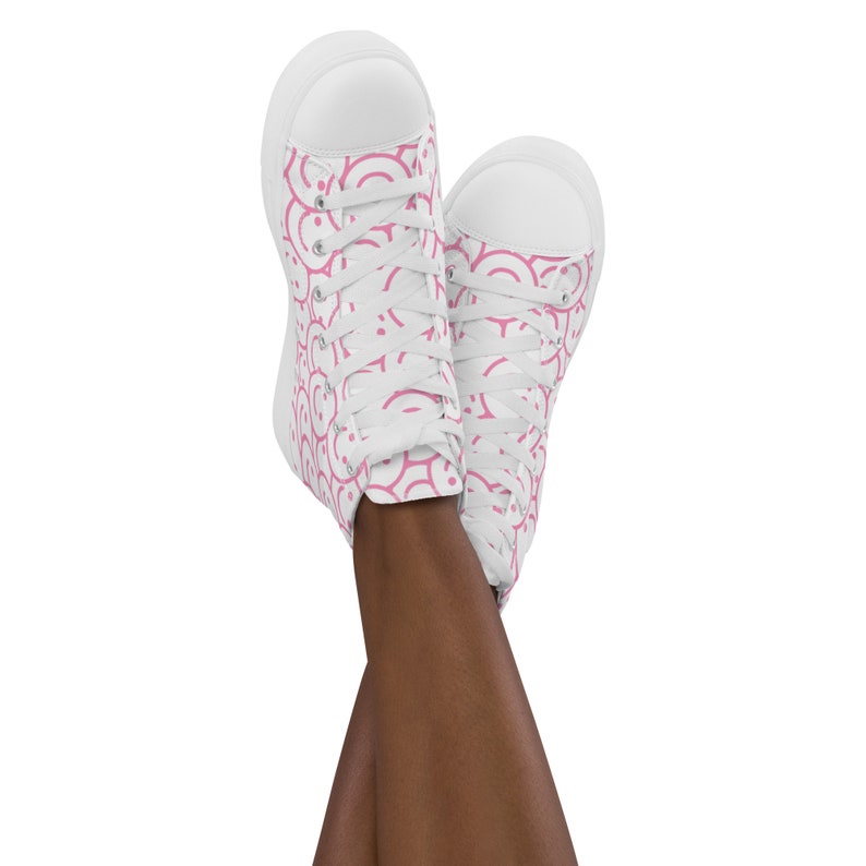 Peut inclure: Baskets montantes blanches avec un motif rose r&eacute;p&eacute;titif. Le motif est compos&eacute; de demi-cercles roses. Les baskets ont des lacets blancs et une semelle en caoutchouc blanche. Les chaussures sont pr&eacute;sent&eacute;es avec les pieds crois&eacute;s.