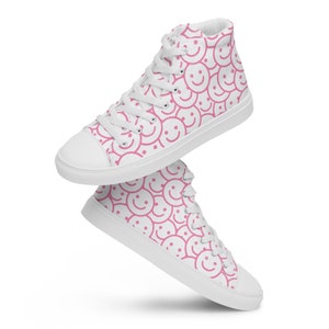 Peut inclure: Baskets montantes blanches avec un motif r&eacute;p&eacute;t&eacute; de visages souriants roses. Les chaussures ont des lacets blancs, un bout de pied blanc et une semelle blanche. Ces baskets d&eacute;contract&eacute;es ont un design joyeux et ludique.