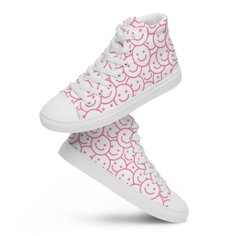 Peut inclure: Baskets montantes blanches avec un motif r&eacute;p&eacute;t&eacute; de visages souriants roses. Les chaussures ont des lacets blancs, un bout de pied blanc et une semelle blanche. Ces baskets d&eacute;contract&eacute;es ont un design joyeux et ludique.