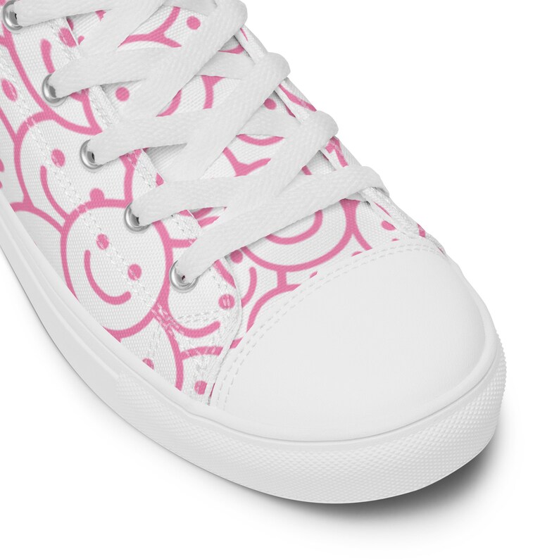 Peut inclure: Baskets montantes en toile blanche avec un motif de visages souriants roses. La chaussure est dot&eacute;e de lacets blancs et d'un embout en caoutchouc blanc. Les visages souriants roses sont r&eacute;partis sur la surface de la chaussure.