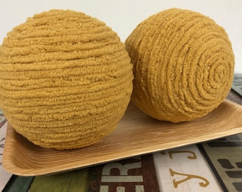 May include: Two mustard yellow round decorative cushions with a textured, fuzzy surface. The cushions are on a wooden tray.