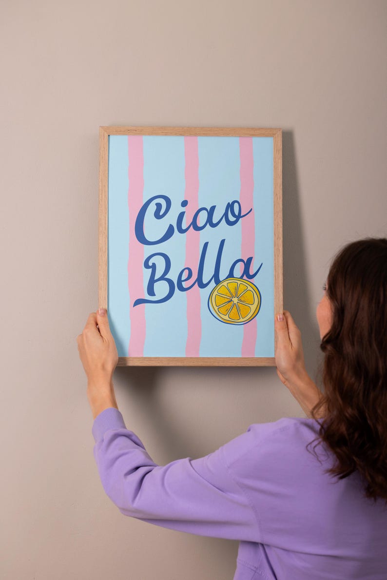 May include: A framed print with a blue and pink striped background. The print says "Ciao Bella" in blue cursive lettering with a yellow lemon slice graphic.