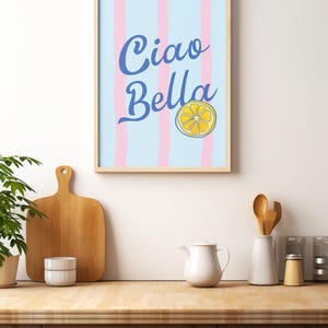May include: A framed print with a blue and white striped background and the text "Ciao Bella" in blue cursive lettering. A yellow lemon slice is centered below the text.