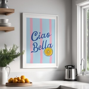 May include: A white framed print with a blue and pink striped background. The print says "Ciao Bella" in blue cursive lettering with a yellow lemon slice graphic.