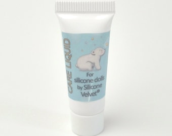 May include: A white tube of Care Liquid for silicone dolls by Silicone Velvet. The tube has a light blue label with a white polar bear illustration and text. The tube is approximately 4 inches tall.