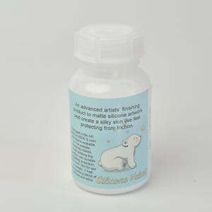 May include: A white plastic bottle with a white cap. The label is light blue with text and a cartoon polar bear illustration. The text reads "Silicone Velvet".
