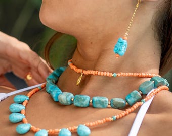 May include: A turquoise and coral beaded necklace and earring set. The necklace features large, rectangular turquoise stones and smaller, teardrop-shaped turquoise beads. The earrings have a single turquoise stone. The set is accented with gold-colored beads.