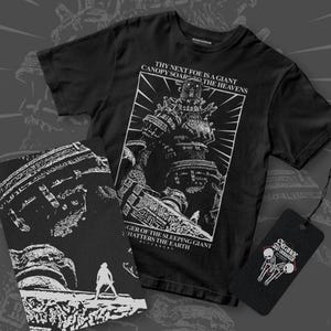 Può includere: Maglietta nera con una grafica bianca di un robot gigante con il testo "Thy next foe is a giant canopy soars the heavens" e "Anger of the sleeping giant that shatters the earth".