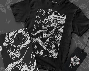 May include: Black t-shirt with a white graphic of a skeletal figure with butterflies and the text "YOU ARE A BEAUTIFUL BUTTERFLY". A matching print and a tag with a skeleton design are also visible.