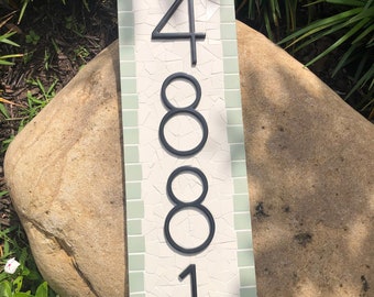 Può includere: Un cartello verticale con il numero civico realizzato con piastrelle di mosaico bianco e verde con numeri neri. I numeri sono 4881.
