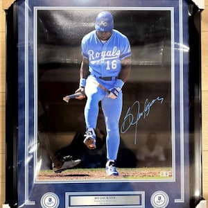 Pode incluir: Foto emoldurada de Bo Jackson com o uniforme do Kansas City Royals, número 16. A imagem mostra Jackson em uma posição de beisebol, com sua assinatura. A moldura é preta com uma borda azul, e a foto inclui o logotipo dos Royals.