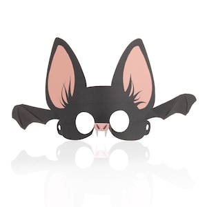 May include: A black bat mask with large, pointed ears and outstretched wings. The mask has eye holes, a pink nose, and small white fangs. The interior of the ears is a light pink color. This mask is perfect for Halloween or costume parties.
